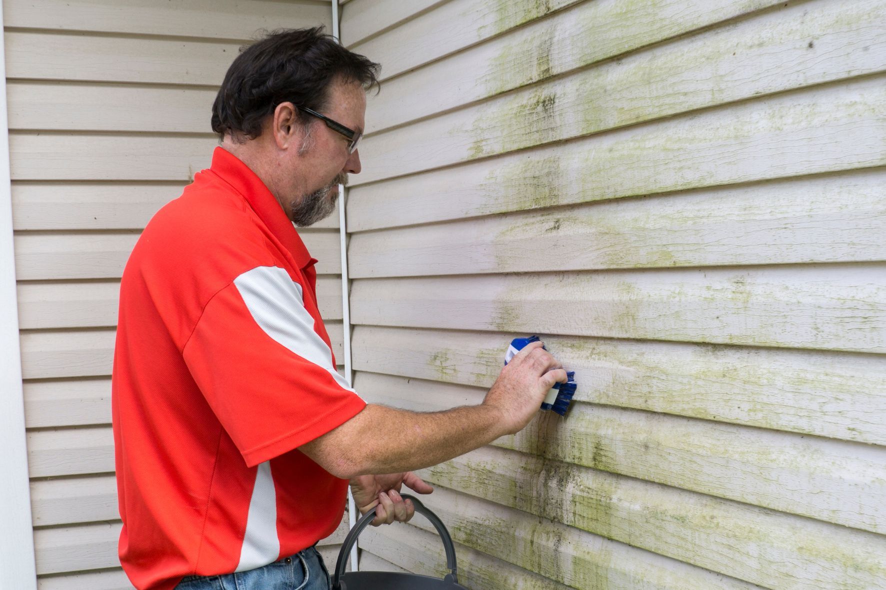 Man cleaning mold from home exterior