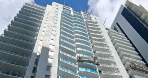 Tall apartment building with many balconies and workers on suspended platforms cleaning the facade.